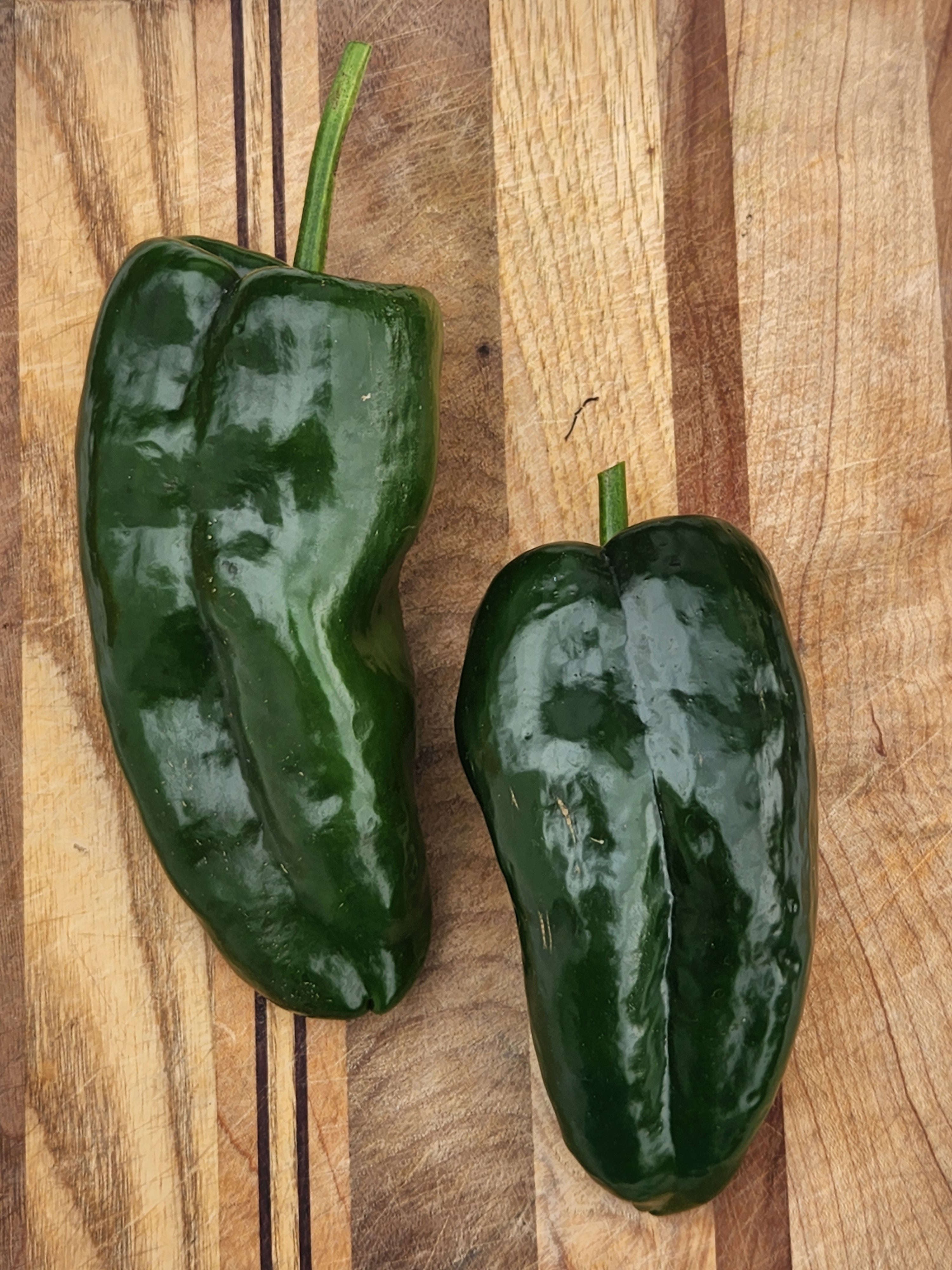 Two green bell peppers on a wooden cutting board